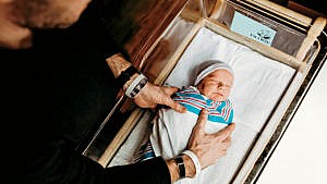 Photo of an adult placing a swaddled newborn in a bassinet at the hospital