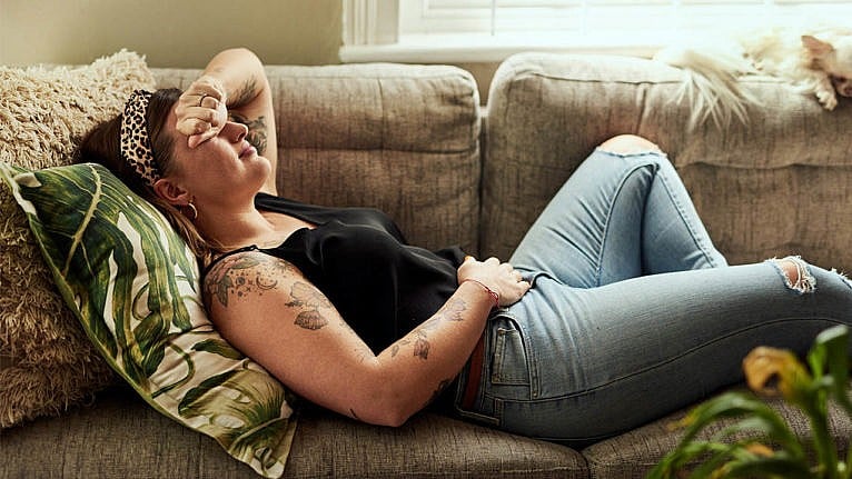 photo of a woman with tattoos lying on a couch with a headache