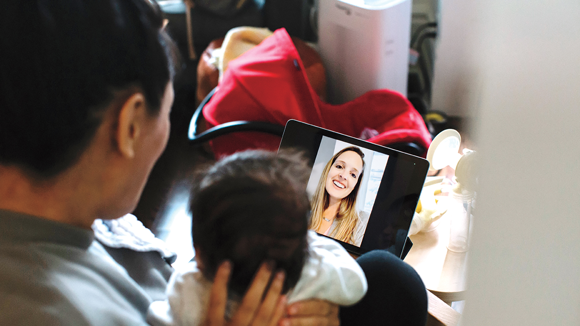 The back of a new mom's head holding up a newborn baby to a smiling woman on an iPad screen for a story on new moms not being ok during the pandemic
