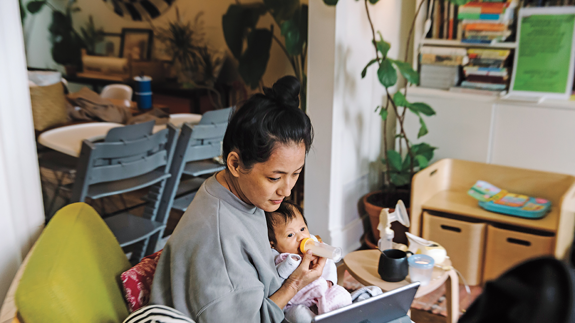 a new mom feeds her tiny baby a bottle while looking at her ipad for a story about new moms not being ok during the pandemic