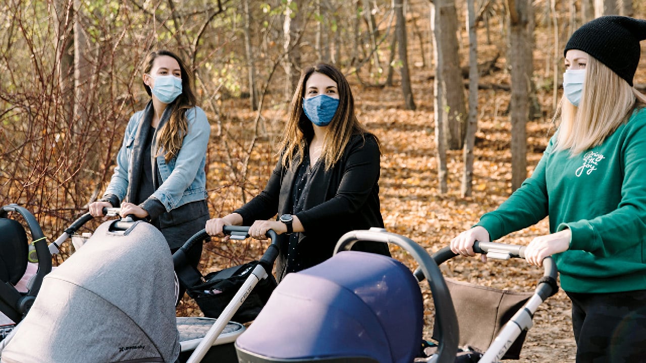 three moms walking in the woods wearing masks while pushing their strollers for a story on how new moms can feel less isolated during the pandemic