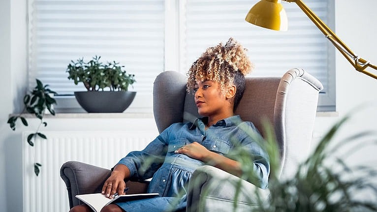 Photo of a pregnant woman sitting in a wingback chair with a thoughtful look on her face