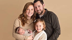 A family portrait showing a couple with their two kids, one is a preschooler and the other is a newborn baby