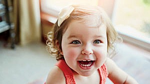 a close up of a smiling toddler with a bow in her hair and a chipped front tooth for a story on what to do if you toddler chips, cracks or knocks out a baby tooth