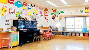 An empty daycare classroom with little chairs stacked and bins tucked into cubbies under the window with cutouts of bright animals and buses on the walls for a story about daycare closures