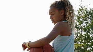 a young girl looking at her yellow apple watch while holding a basketball