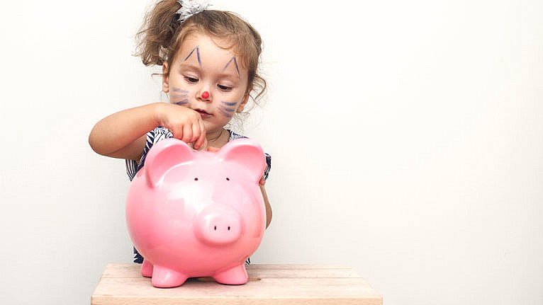 A little girl with cat facepaint puts a coin into a big pink piggy bank for a story on RESPs