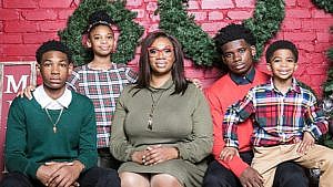 A holiday photo of a mom in a green dress surrounded by her three sons and two daughters all wearing red and green for a story on how she handles teaching virtual school and caring for her four kids