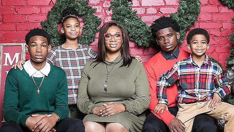 A holiday photo of a mom in a green dress surrounded by her three sons and two daughters all wearing red and green for a story on how she handles teaching virtual school and caring for her four kids