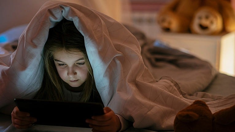 Photo of a kid in bed playing with a tablet under the covers