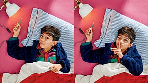 Photo of a kid laying in bed while holding a thermometer up to a light bulb and a finger to his mouth saying shhh