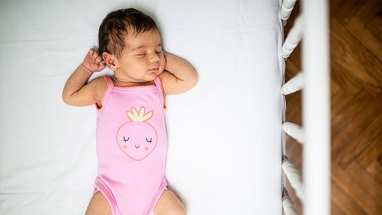 Photo of a baby in a pink onesie sleeping in a crib