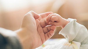 A newborn baby's hand grasping a parent's finger for a story on newborn reflexes