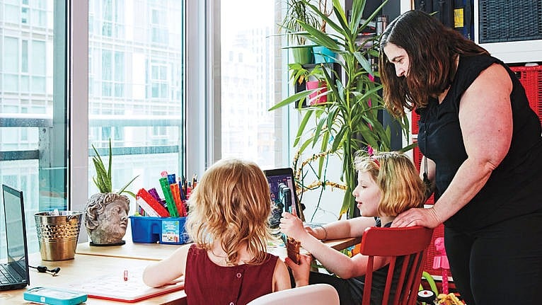 Photo of a mom looking over her kids' shoulder while they sit at a desk and play with a tablet