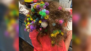 Photo of a kid with multiple brightly coloured toys tangled in her hair