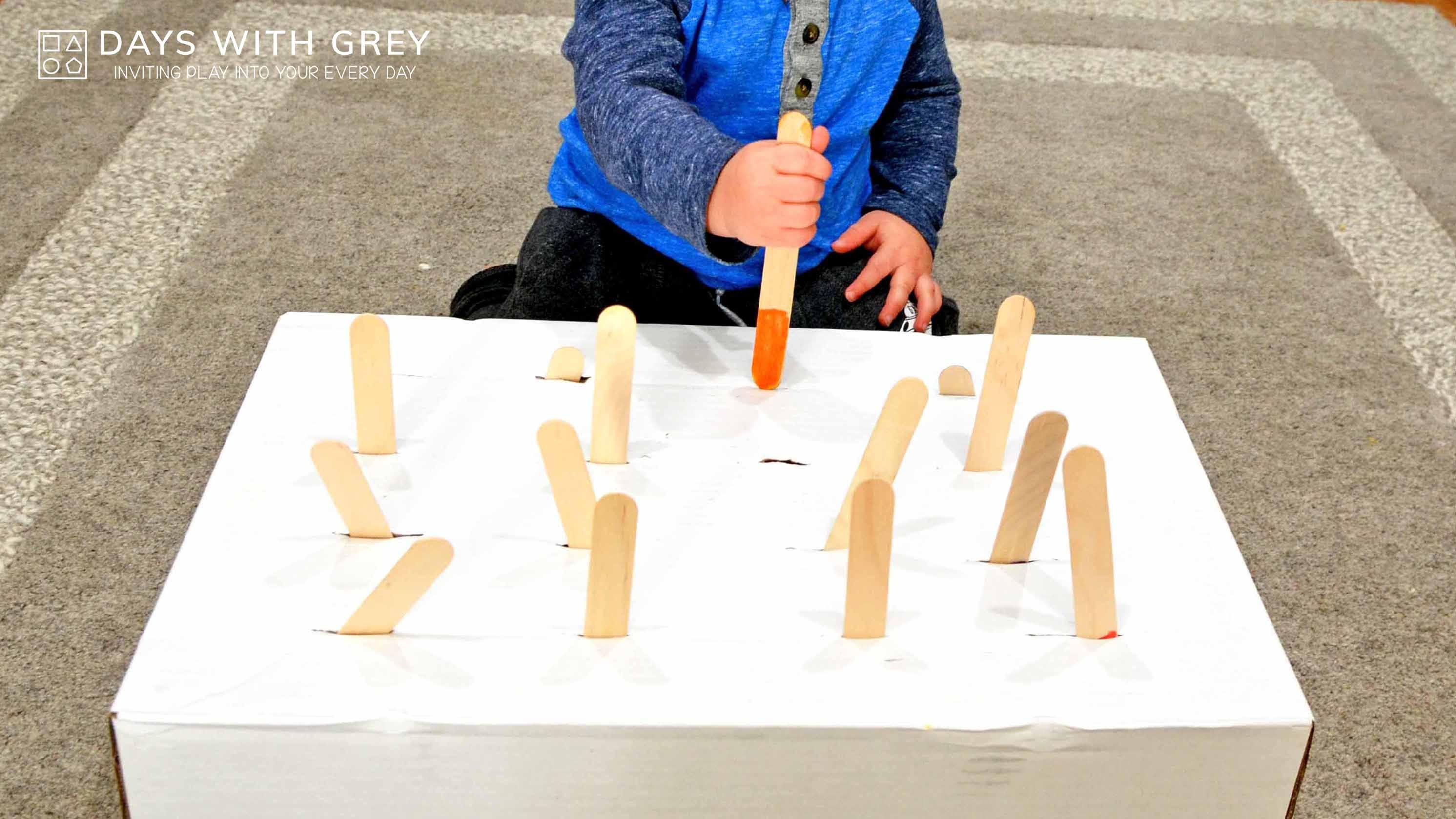 a child pokes popsicle sticks into a box with slits for a story on toddler activities you can set up the night before