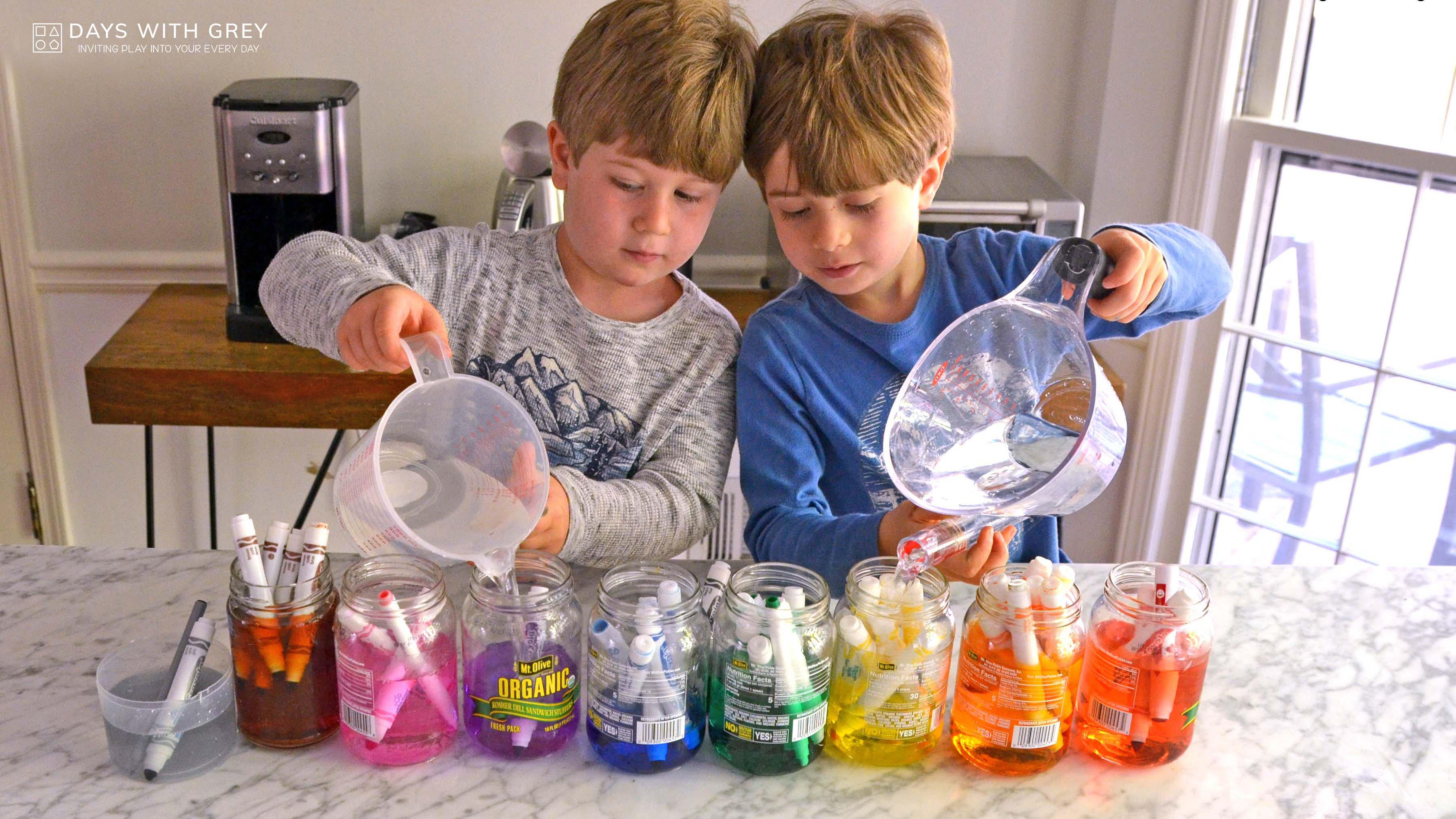 Two young boys pour water into various containers each with different coloured markers for a story on toddler activities you can set up the night before