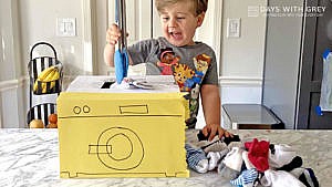 A young boy puts socks into a cardboard washing machine using tongs for a story on toddler activities you can set up the night before