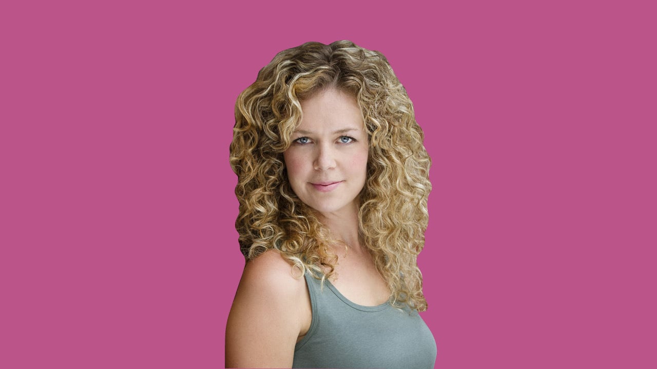 Workin' Moms star Juno Rinaldi wearing a grey tank top and posing in front of a pink background