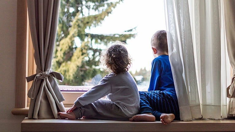 Photo of two kids sitting at the window wearing pajamas looking outside