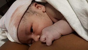 A close up of a newborn baby lying on his mother's chest covered in a blanket for a story on delivering as a Black woman with a Black nurse
