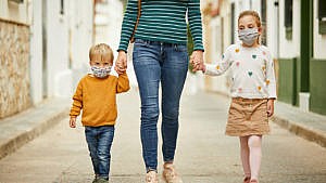 Photo of a mom and two kids walkiing down a street wearing masks