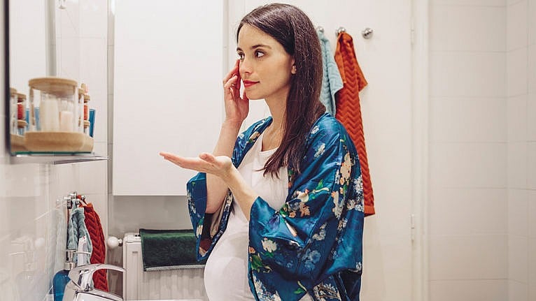 Photo of a pregnant person in a bathroom putting skincare on their face