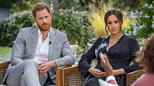 Prince Harry and Meghan Markle seated on an outdoor patio with greenery behind them during their interview with Oprah