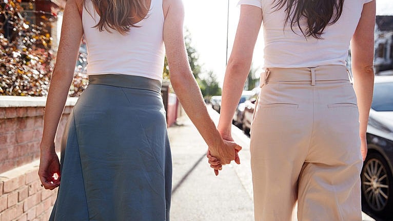 Two women dressed in tailored outfits from behind walking hand in hand for a story on a woman who came out as queer in her late 30s