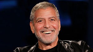 George Clooney smiling at the camera in a leather jacket