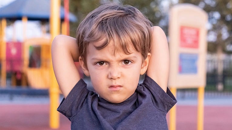 a little boy at the playground with his arms over his head staring at the camera with an angry look