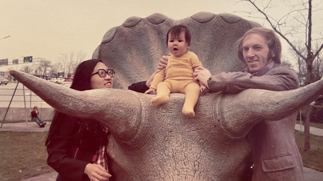 A retro photograph of two parents with their baby sitting on a statue of a triceratops