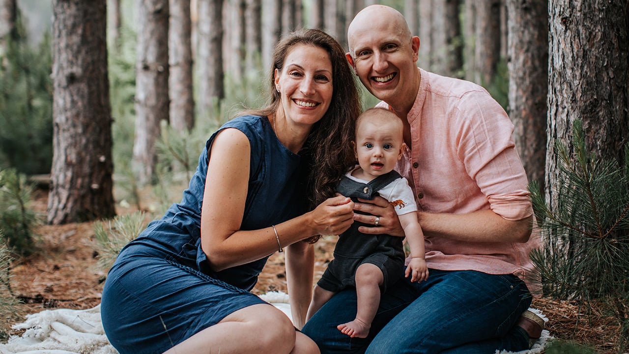 A couple pose on a blanket in the woods with their baby