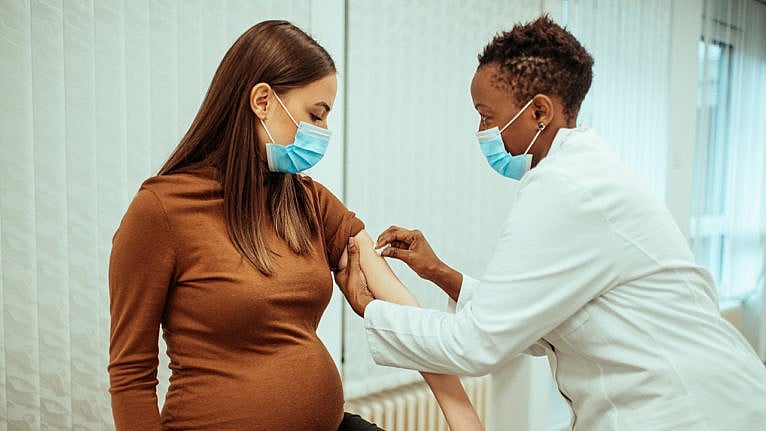 A pregnant woman wearing a mask receives a vaccine from a doctor in a mask