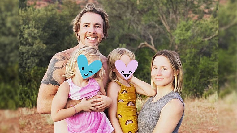 Photo of Kristen Bell, Dax Shepard and their two daughters posing for a family pic outside. Their daughters' faces are covered with heart emoji to protect their identities