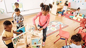 Children play at tables and with a doll house in a brightly coloured daycare for a story on the national childcare plan