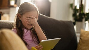 a little girl covers her eyes while watching her tablet for a story on kids watching porn