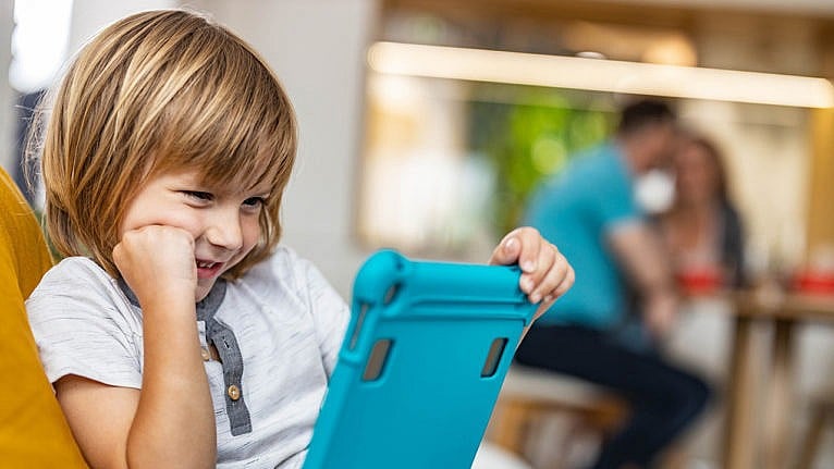 a young boy smiles while looking at his ipad for a story on whether you should worry about your kid's screen time during the pandemic
