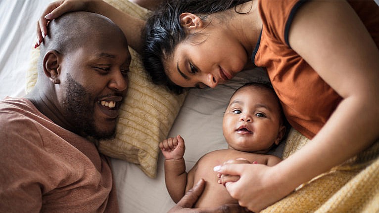 Photo of a couple and their baby laying in bed looking cozy and content