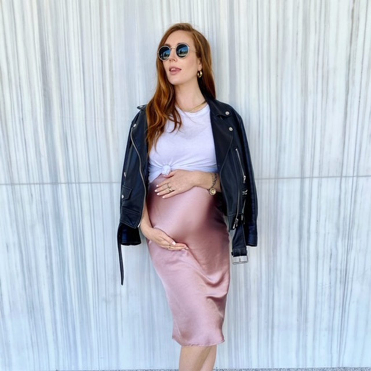 Photo of Jessi Cruickshank holding her baby bump while posing in front of a marble wall