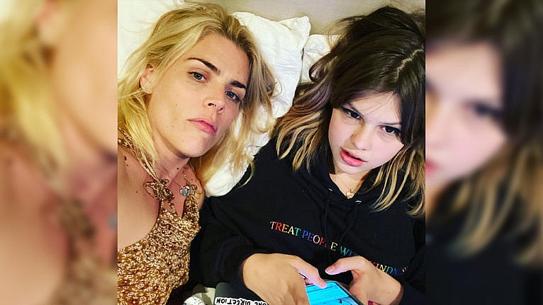 Busy and her kid Birdie relaxing in bed. Birdie is holding a smartphone in their hands