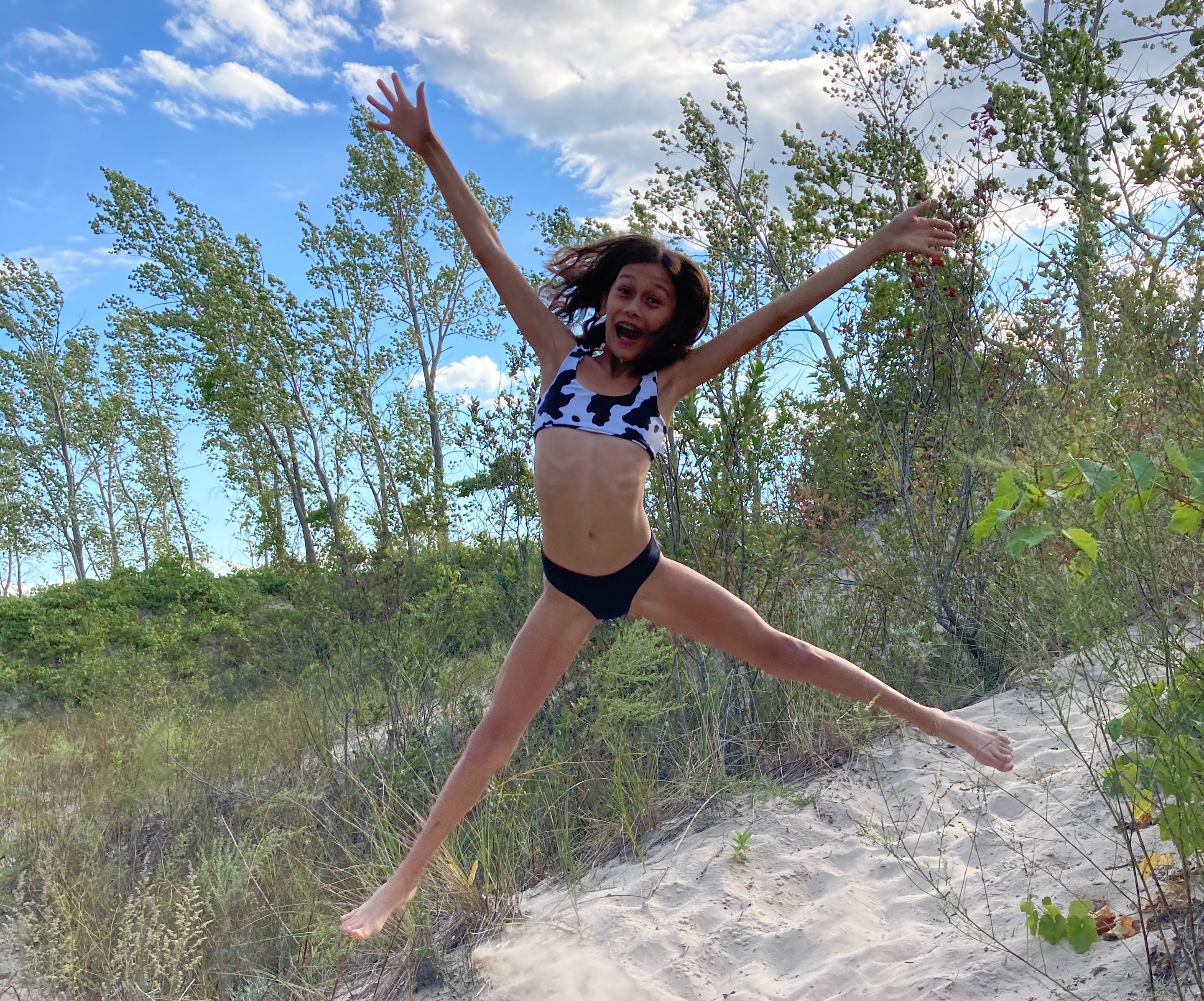young girl in a bikini jumping in grassy sand dune