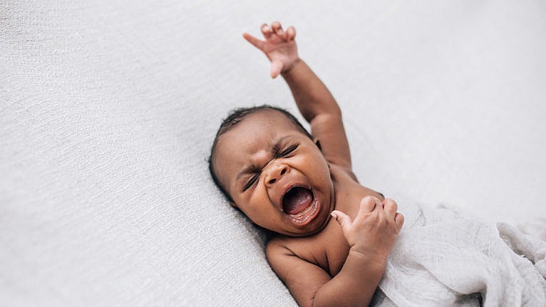 a baby crying with their arm outstretched for a story on colic