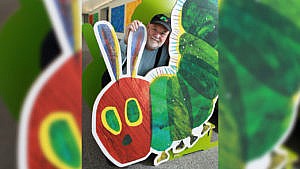 Author and illustrator Eric Carle poses with a large caterpillar cardboard cutout