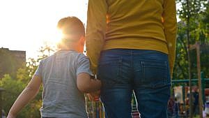 an image showing the backs of a mom and child holding hands standing in front of a playground