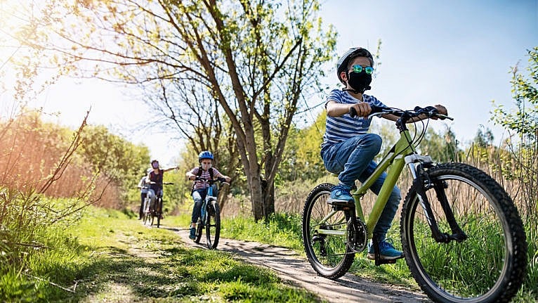Photo of a family biking through a park on a sunny day while wearing face masks