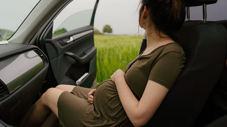 woman clutches pregnant belly in passenger seat of car while looking off into fields