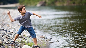 A kid winds back to skip a rock into a river.