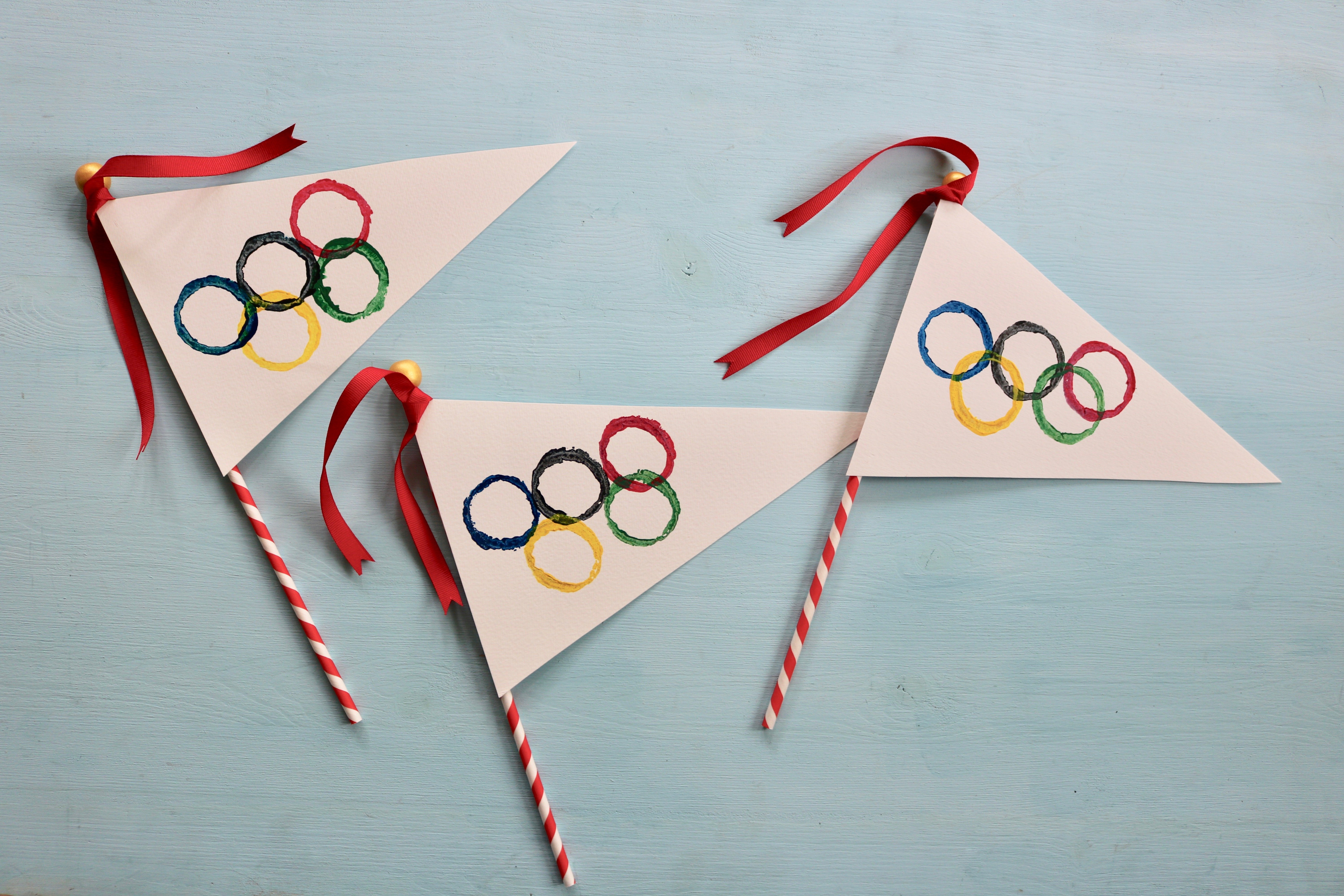 Three handmade flags with Olympic logos on them.