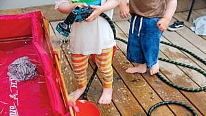 photo of two young kids on a deck playing water and a hose